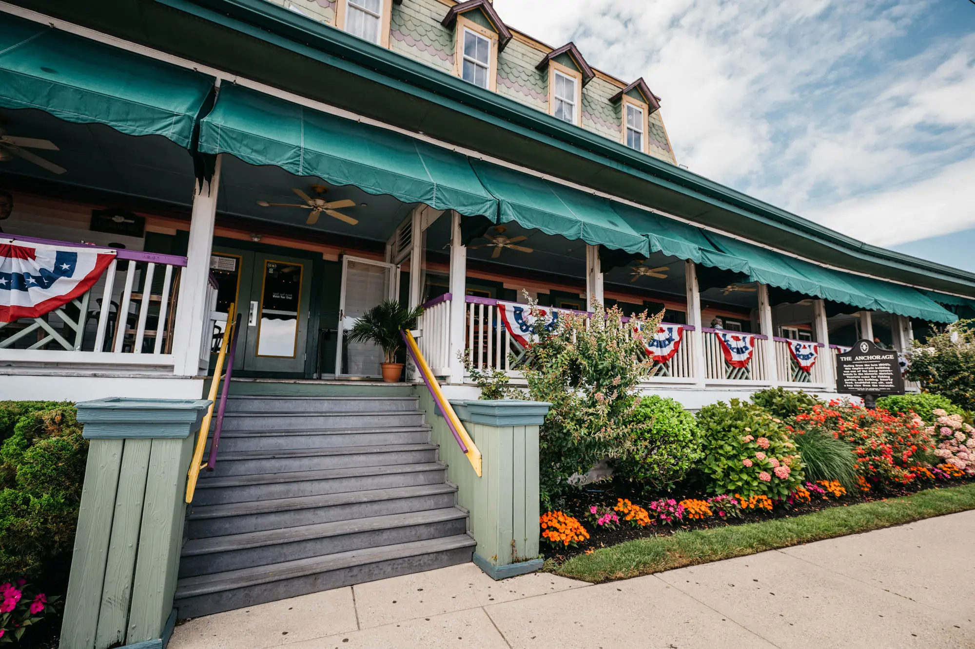 The Anchorage Tavern front porch with green awnings, bunting and flower gardens