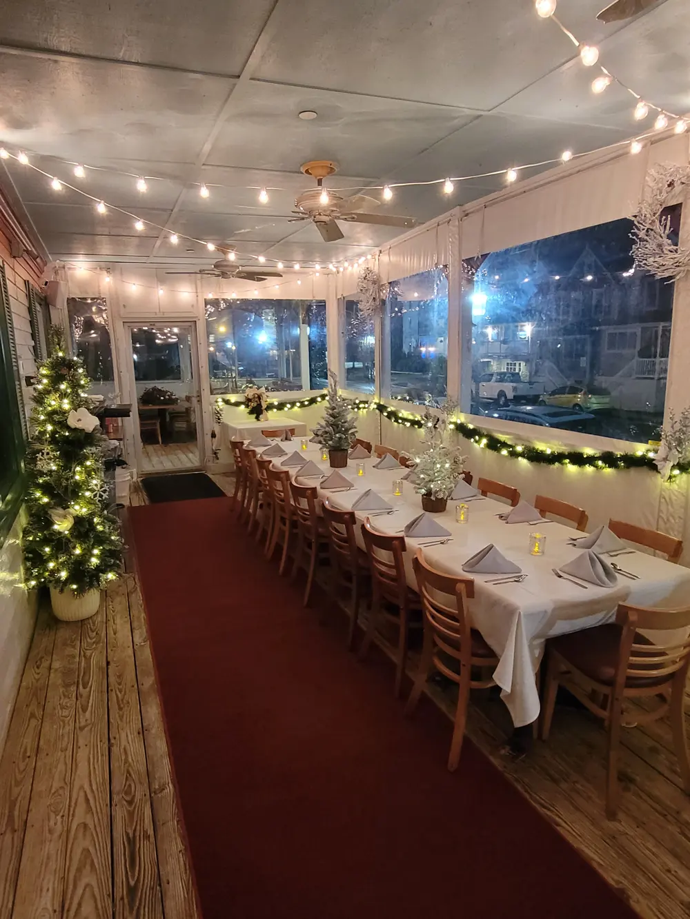 A dining room with white-clothed tables, string lights and holiday greenery