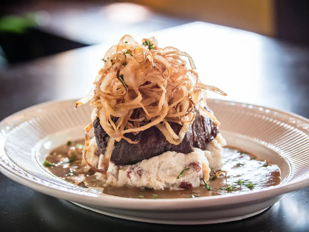 Steak topped with crispy fried onions over mashed potato